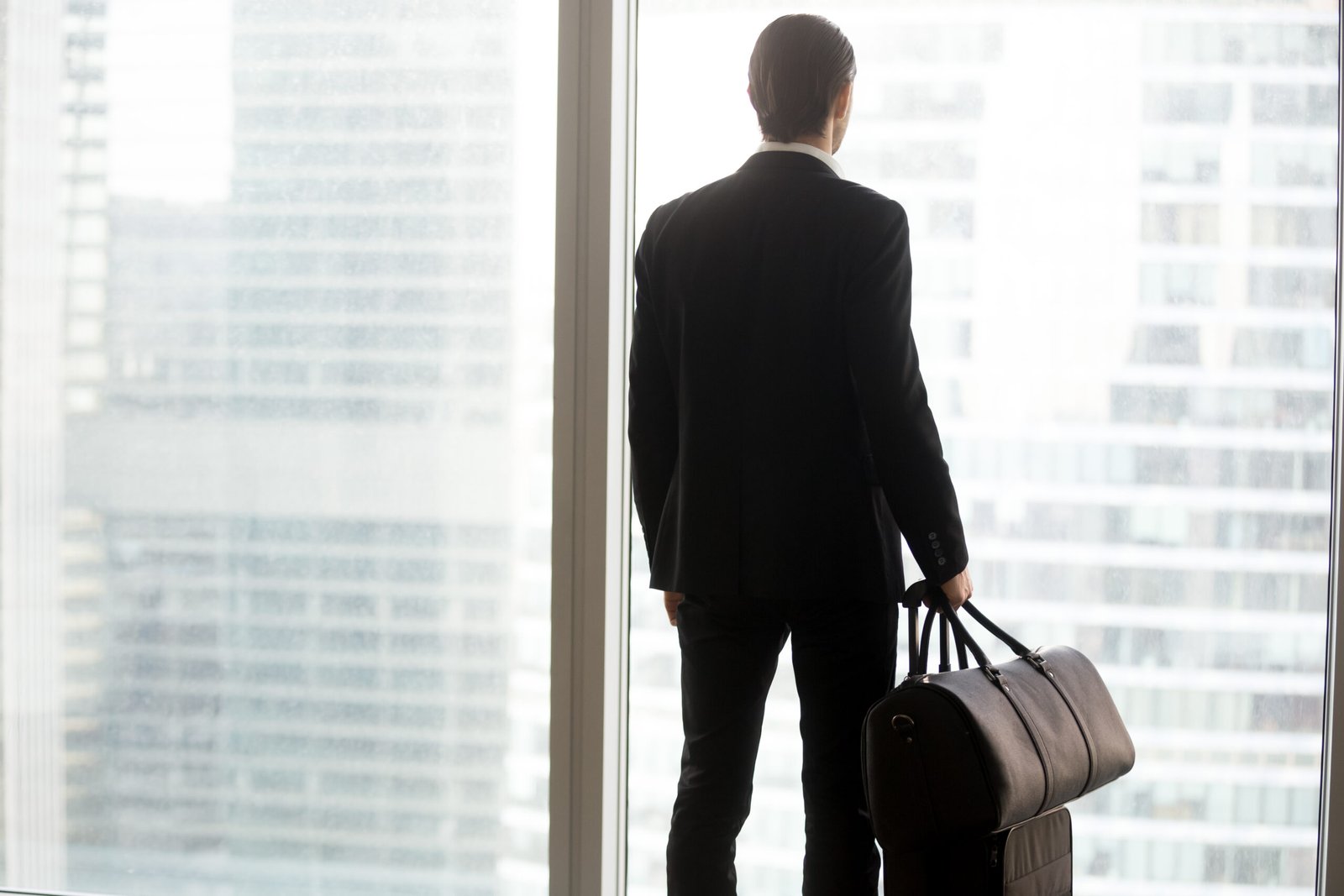 businessman with luggage standing in front of large window.